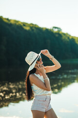 Fototapeta premium Sexy girl talking on the phone in the park.Gorgeous slender brunette talking on the phone by the lake.Smiling woman talking outdoors.