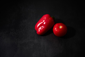 Fresh vegetables on black kitchen table. Minimalistic restaurant menu. Whole wet red bell pepper and tomato on black background.