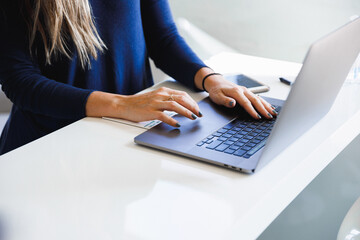 Woman typing using laptop keyboard at her workplace in the morning. Female writing emails online, close-up view from the side