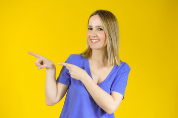Young woman over isolated yellow background pointing fingers to the side