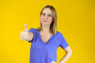 Obraz premium Smiling pretty young woman showing thumb up isolated over yellow background