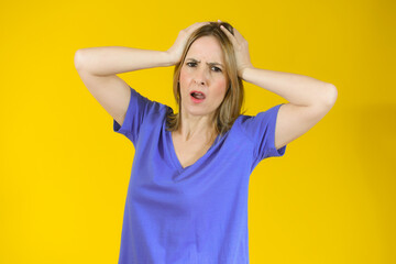 Shocked amazed young woman with hands on head standing over yellow background