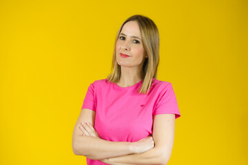 Fototapeta premium Portrait of a smiling young woman standing with arms folded isolated over yellow background