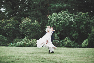 Romantic, fairytale, happy newlywed couple hugging and kissing in a park, trees in background