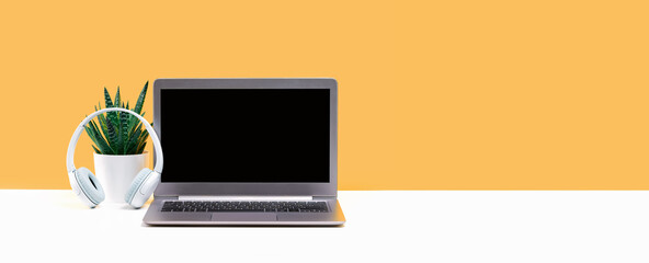 Laptop. Mockup screen and headphones on white desk and plain yellow background banner. Distant...