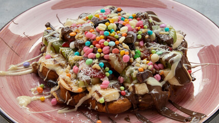 Waffles with lots of candies on a gray background and a pink plate