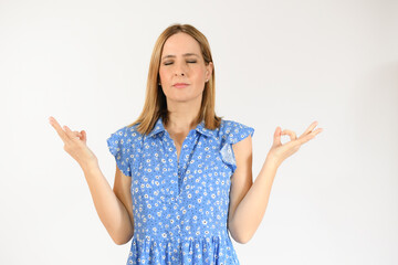 Woman meditates indoor, keeps hands in mudra gesture, has eyes closed over white background.