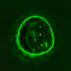 Clear transparent liquid gel dark green drop or smear with neon light green flare isolated on dark green background. Top view. Virus protection or cosmetics concept. Serum texture