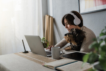 Young business woman working on laptop computer with pet dog inside home office - Focus on face