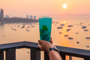 Woman holding a cup of refreshing blue mojito cocktail with mint leaves in a rooftop bar in Thailand