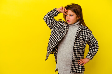 Little caucasian girl isolated on yellow background looking far away keeping hand on forehead.