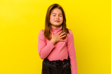 Little caucasian girl isolated on yellow background laughs out loudly keeping hand on chest.