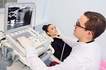 the doctor performs an ultrasound examination of the thyroid gland of a young, pretty woman in a modern clinic. Prevention of thyroid cancer.