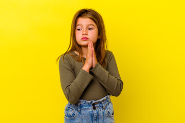 Little caucasian girl isolated on yellow background praying, showing devotion, religious person...