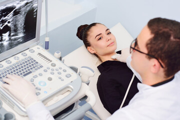 the doctor performs an ultrasound examination of the thyroid gland of a young, pretty woman in a...