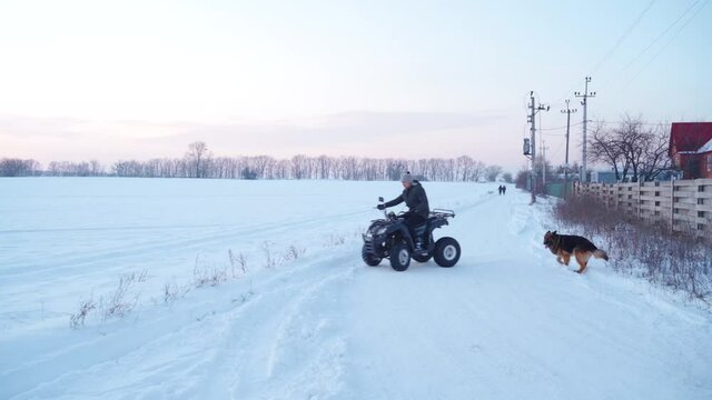 The guy is riding on an ATV in the snowy field