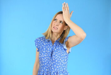Fototapeta premium Young woman standing over blue isolated background clueless and confused expression with hand on head. Doubt concept.