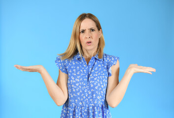 Young woman standing over blue isolated background clueless and confused expression with arms and hands raised. Doubt concept.