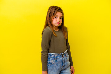 Little caucasian girl isolated on yellow background shrugs shoulders and open eyes confused.
