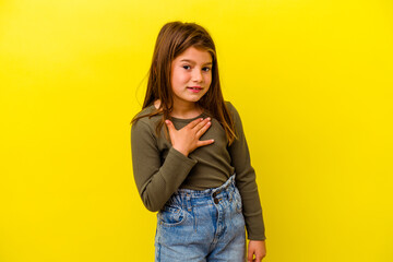 Little caucasian girl isolated on yellow background laughs out loudly keeping hand on chest.