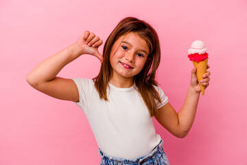 Little caucasian girl holding ice cream isolated on pink background feels proud and self confident, example to follow.