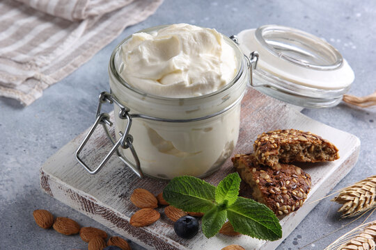 Fermented milk product. Healthy yogurt with cereals in a transparent jar on a white wooden board with nuts, mint and ears on a light grey background. Background image, copy space