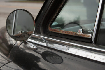 Old black car with chrome details; vintage round side view mirror and window
