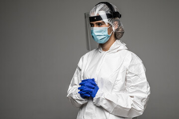 Woman doctor wearing white hazmat suit goggles medical gloves and respirator standing isolated on gray background