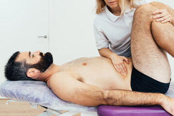 Bearded male patient lying on the stretcher in the physiotherapy clinic is treated for abdominal...