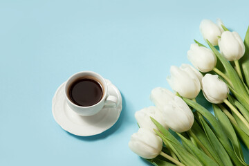 Cup of coffee and white tulips on a blue background. Spring coffee concept. top view, flat lay.