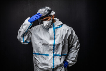 Tired man doctor wearing hazmat suit on black background. Medical specialist exhausted from infectious disease pandemic