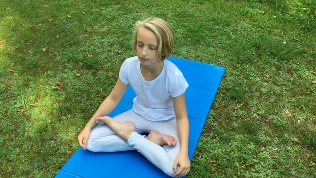 Beautiful blonde kid girl of school age does yoga on a mat in the park