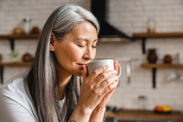 Nice-looking caucasian mature woman drinking hot coffee in the kitchen