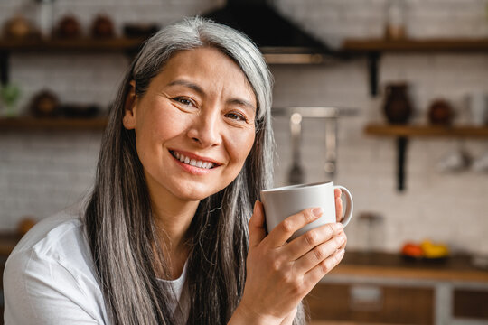 Cheerful mixed-race woman with grey hair drinking tea in the kitchen