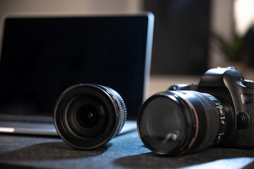 Close up of a professional digital camera and lens on the desktop of a photographer with a laptop.