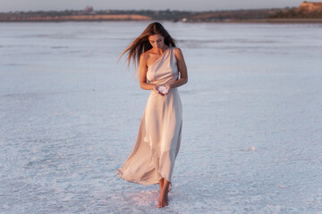 Young blonde woman in evening airy pastel pink powdery dress, holds pieces of crystallized white...