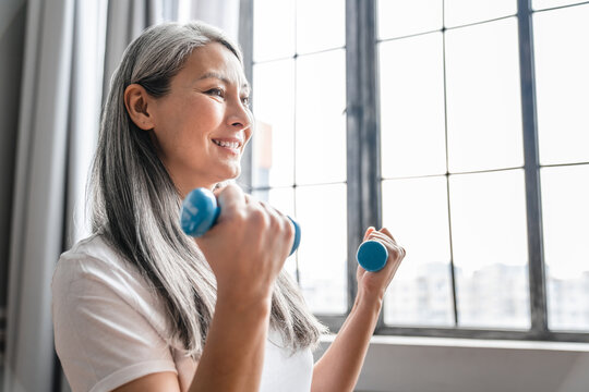 Side view photo of a mature grey-haired woman exercising with dumbbells