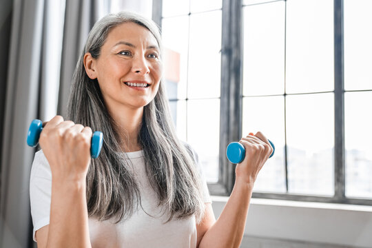Sporty caucasian middle-aged woman doing physical exercises with dumbbells