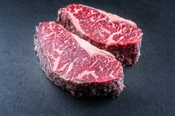 Raw dry aged wagyu roast beef steak offered as close-up on a black board with copy space