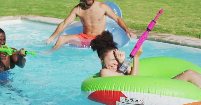 Diverse group of friends having fun playing with water guns on inflatables in swimming pool