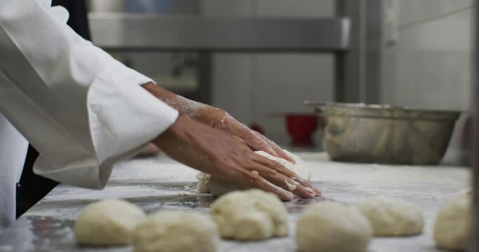 Midsection of mixed race female chef preparing dough adding flour