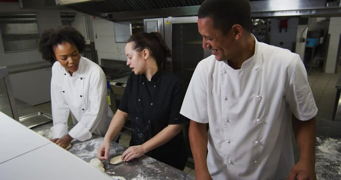 Diverse group of chefs preparing dough and talking in restaurant kitchen