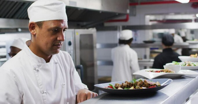 Caucasian male chef garnishing dish and smiling in restaurant kitchen