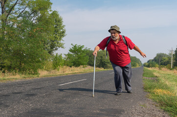chubby bearded  senior hiker moving fast using walking stick on a roadside in Ukrainian rural area at summer time