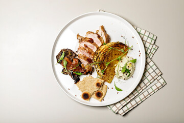 Duck breast with cabbage steak, cheese sauce and rye flatbread. Delicious restaurant dish on a round plate on a checkered napkin. Top view