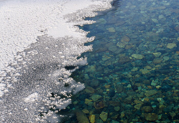 Texture of pebble river bottom with white mosaic ice.