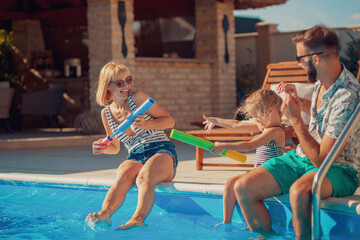 Parents and child playing with squirt guns by the pool