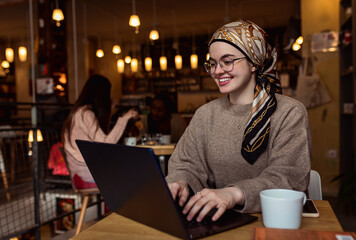 Portrait of young middle eastern woman using laptop in coffee shop.