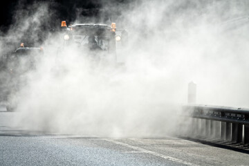 Sweeping the freeway after winter, road service. A special tractor (road sweeping machine) with a cylindrical broom sweeps the roadside, car raised quite a dust.