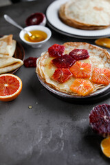 Thin pancakes with honey and blood oranges on a gray table. Treats at the Maslenitsa.